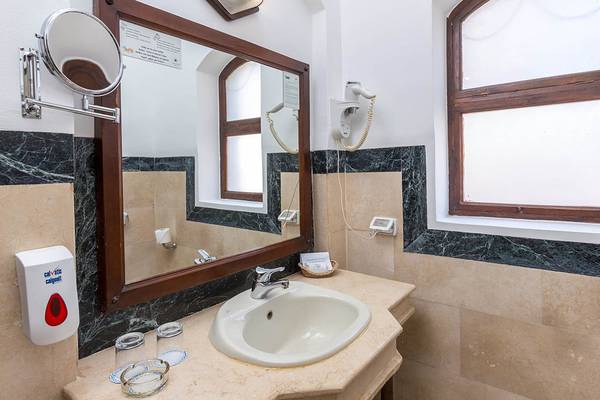 Badezimmer im Sultan Bey Resort mit Spiegel, Waschbecken, Föhn und Fenster.