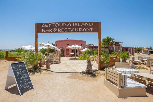 Eingang zum Zeytouna Island Bar & Restaurant mit blauem Himmel und weißen Sonnenschirmen.