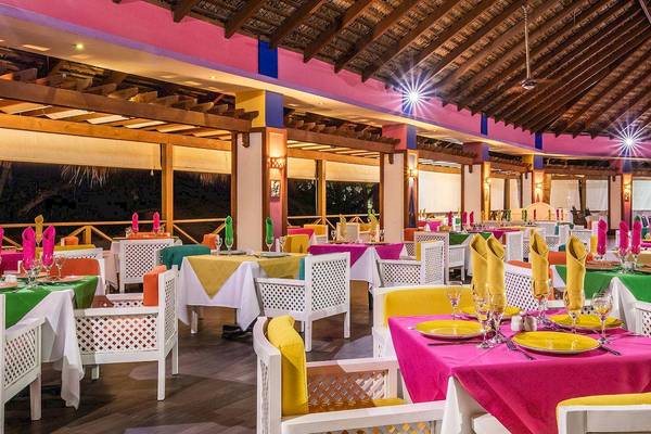 Marien Puerto Plata Hotel Innenrestaurant mit bunten Tischen und Stühlen, dekoriert mit bunten Tischdecken und serviert mit Gläsern und Besteck.