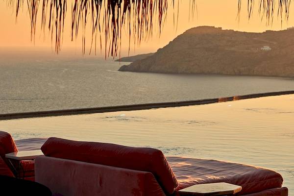 Sonnenuntergangsansicht vom Pool der Myconian Villa Collection mit Meer und Bergen im Hintergrund.