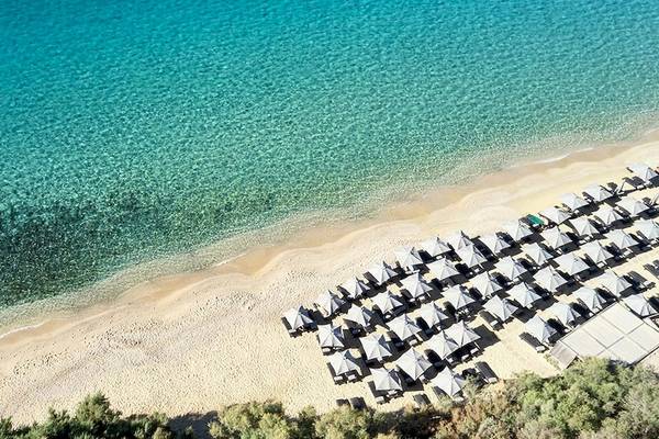 Luftaufnahme des Myconian Villa Collection Strands mit kristallklarem Wasser und vielen Sonnenschirmen.
