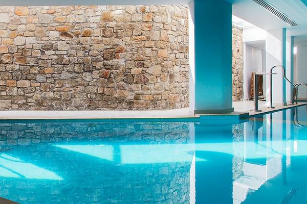 Innenansicht des Schwimmbads des Myconian Villa Collection Hotels mit blauem Wasser und Steinwand