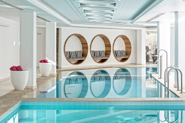 Innenpool im Myconian Villa Collection Hotel mit drei Holzsesseln und blauem Wasser.