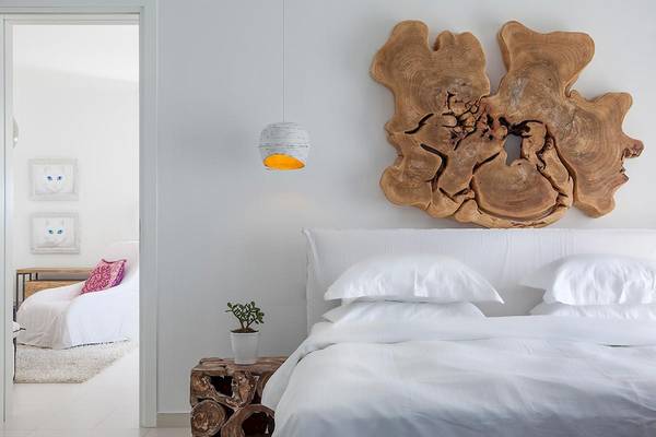 Schlafzimmer der Myconian Villa Collection mit weißen Laken, Kissen und Holzdekor.