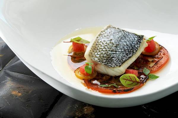 Ein Fischgericht in einem weißen Teller mit Tomaten und grünen Blattgemüse