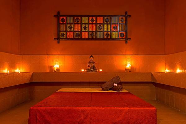 Spa-Zimmer im Le Meridien Abu Dhabi mit Buddha-Statue, Kerzen und rotem Bett.
