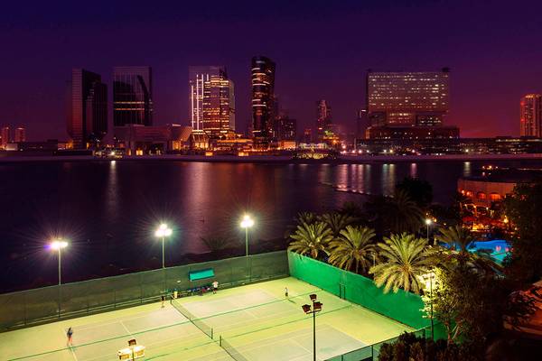 Abendlicher Ausblick auf die Stadt von Le Meridien Abu Dhabi mit Tennisplätzen und einer beleuchteten Skyline.