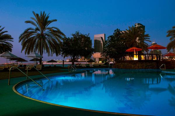 Der beleuchtete Pool des Le Meridien Abu Dhabi bei Nacht mit Palmen und Blick auf die Skyline.