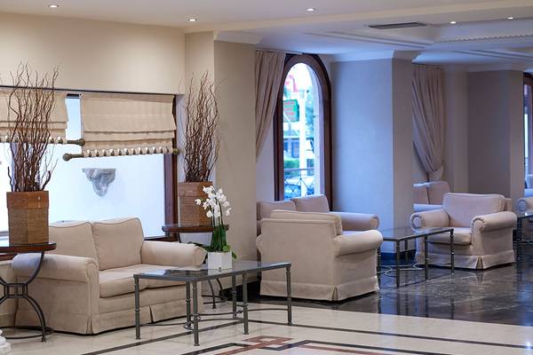 Lobby des Mitsis Petit Palais Beach Hotels mit beige Möbeln und großen Fenstern.
