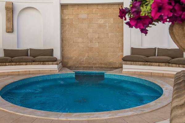 Schwimmbecken im Freien des Mitsis Petit Palais Beach Hotels mit braunen Kissen und einer Blumenvase