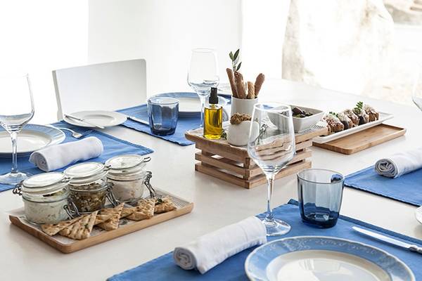 Ein Tisch im Grecotel Mykonos Blu, gedeckt mit weißen Tellern, Gläsern und blauen Tischdecken.