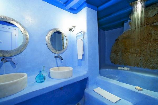 Badezimmer im Grecotel Mykonos Blu mit blauen Wänden, zwei Waschbecken, Spiegeln und einer Regendusche.