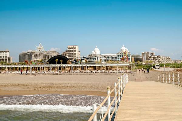 Strandansicht des Adalya Elite Lara Hotels mit Gebäuden und Pavillons im Hintergrund.