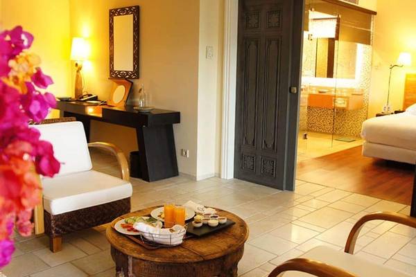 Hotelzimmer im Marmara Bodrum mit Esstisch, Sessel, Tischlampe und Schlafzimmer.