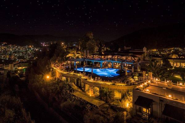 Nachtansicht des Marmara Bodrum Hotels mit Pool und Stadt im Hintergrund