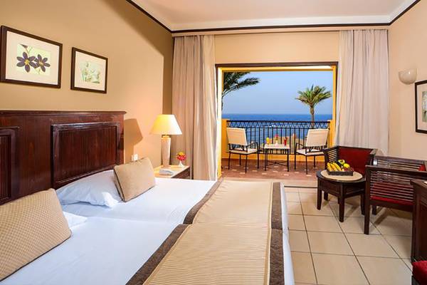 Hotelzimmer des Jaz Samaya Resort mit Meerblick, Balkon, zwei Betten, Tisch, Fernseher und Dekor.