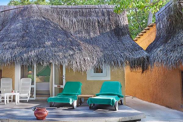 Kuredu Island Resort & Spa mit einer strohgedeckten Hütte und grünen Liegestühlen auf einer Holzterrasse.