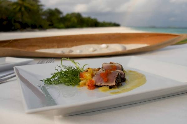 Gericht auf einem weißen Teller mit Meeresfrüchten und Beilagen auf einem Tisch am Strand des Kuredu Island Resorts.