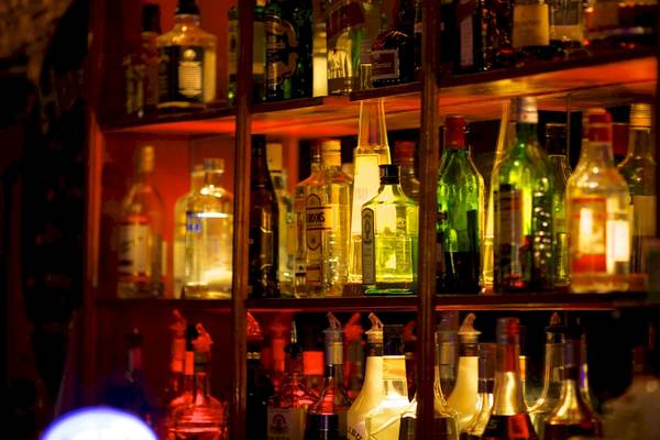 Regal mit verschiedenen Alkoholflaschen, die in einem dunklen Raum beleuchtet sind.