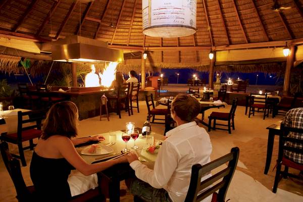 Ein Paar sitzt bei einem Tisch im Innenbereich des Kuredu Island Resorts und Spa, bei Nacht.