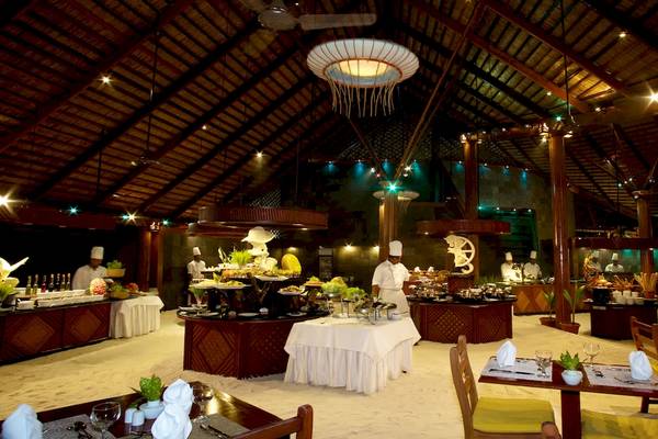 Innenbereich des Restaurants im Kuredu Island Resort & Spa mit gedeckten Tischen und Köchen, die Speisen zubereiten.