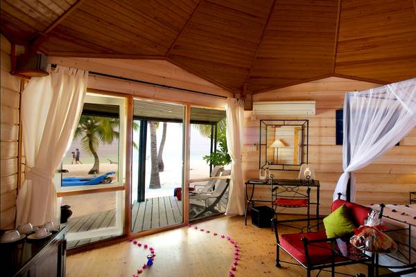 Innenansicht des Kuredu Island Resort & Spa Zimmers mit Doppelbett, offenem Balkon und Meerblick.