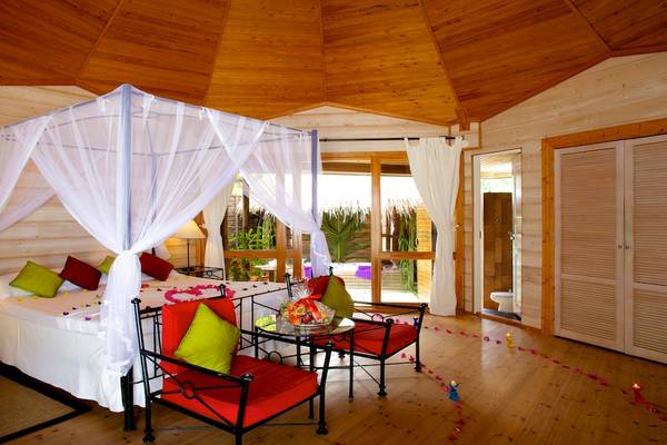 Schlafzimmer im Kuredu Island Resort & Spa mit Himmelbett, roten Stühlen und Fenstern, die auf einen Garten blicken.