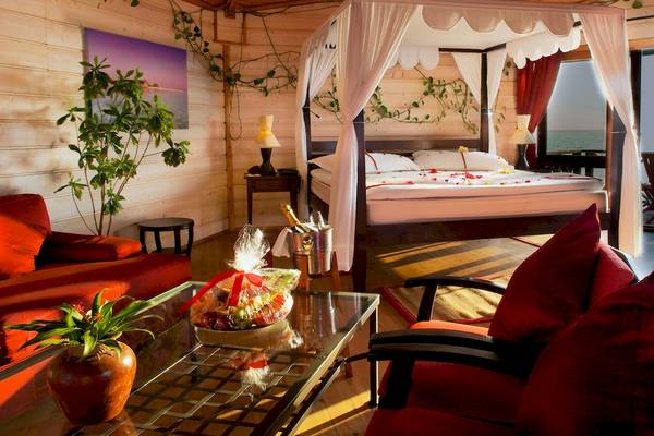 Luxuriöses Schlafzimmer im Kuredu Island Resort & Spa mit Baldachin-Bett, roten Kissen und Blick auf das Meer.