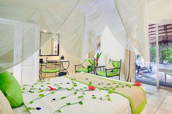 Ein Zimmer im Kuredu Island Resort & Spa mit einem Bett, grünen Kissen, und einem Balkon mit Aussicht auf die Natur.