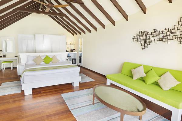 Schlafzimmer im Kuredu Island Resort & Spa mit weißen Möbeln, grünem Sofa und Holzboden.