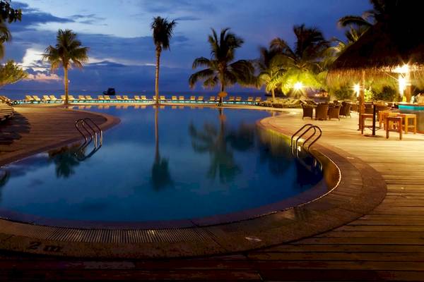 Nachtansicht des Außenpools des Kuredu Island Resort & Spa mit illuminierten Palmen und Liegestühlen