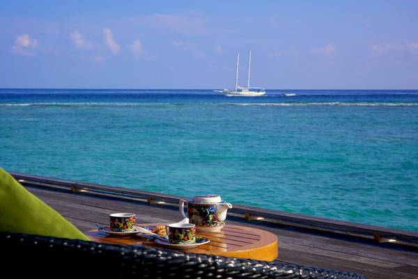 Meerblick von der Terrasse des Kuredu Island Resorts & Spa mit einem Tisch, Tassen und einem Segelboot im Hintergrund.