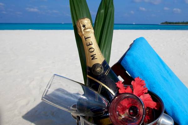 Eine Flasche Moet in einem Eiskubel mit Gläsern und Blumen auf einem Strand von Kuredu Island Resort & Spa