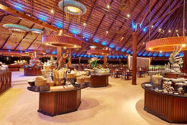 Innenansicht des Restaurants im Kuredu Island Resort & Spa mit vielen Tischen und Stühlen, Buffettischen und dekorativen Beleuchtungskörpern.