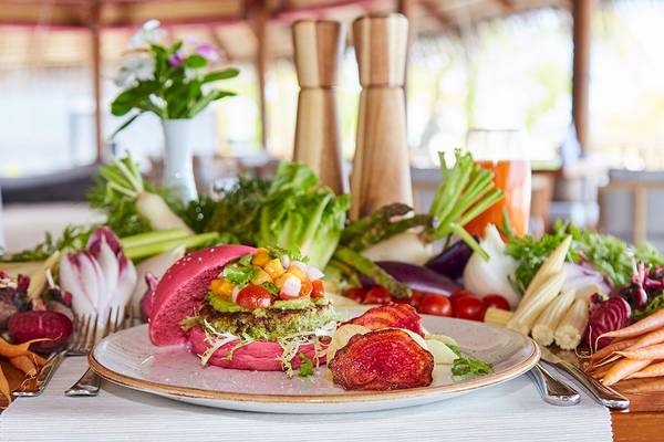 Gedeckter Tisch im Kuredu Island Resort & Spa mit einem bunten Burger, Gemüse und Getränken.