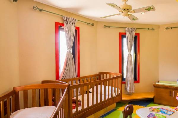 Kinderzimmer im InterContinental Resort Mauritius mit zwei Babybetten, Deckenventilator und bunten Teppich.
