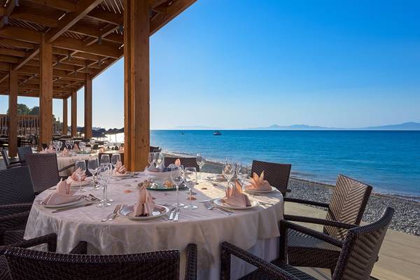 Terrasse des Avra Beach Resort Hotels und Bungalows mit Blick auf das Meer und gedeckten Tischen.