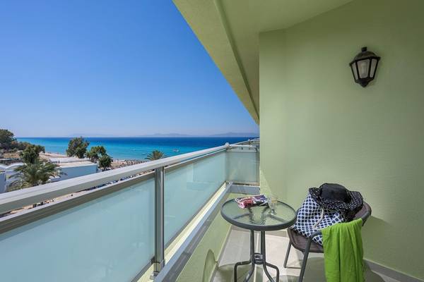 Balkon des Avra Beach Resort Hotels mit Blick auf das Meer, ein Tisch mit Zeitschriften und eine Lampe an der Wand.