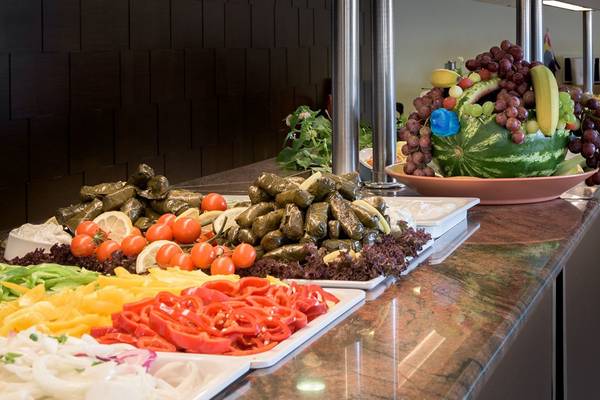 Buffet-Tisch mit verschiedenen Gemüsesorten und Obst, einschließlich Tomaten, Paprika, Salat, Auberginen und einem Wassermelonenkorb mit Früchten.
