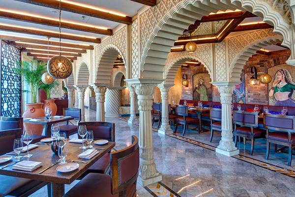 Innenansicht des Restaurants im Dukes The Palm, einem Royal Hideaway Hotel mit runden Bögen, gedeckten Tischen und Wandmalereien.