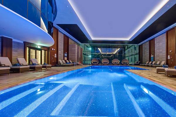 Innenpool des Dukes The Palm, ein Royal Hideaway Hotel mit gepolsterten Liegestühlen und Holzboden.