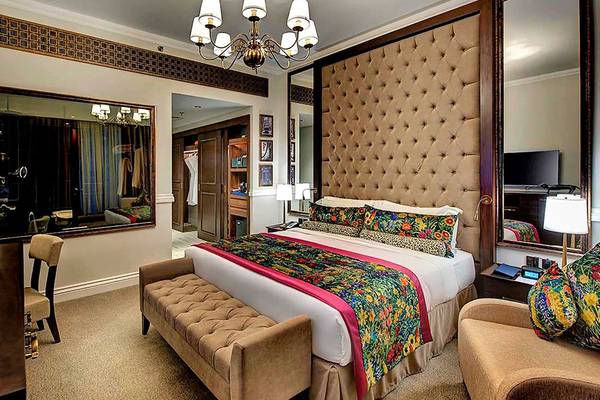 Innenansicht des Schlafzimmers im Dukes The Palm, einem Royal Hideaway Hotel mit Bett, Spiegel, Deckenleuchte, Schreibtisch und Stühlen.