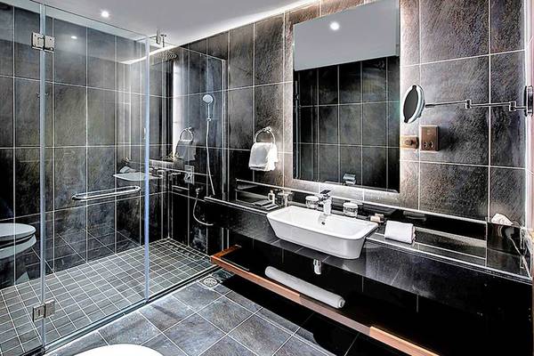 Schwarz gefliestes Badezimmer im Dukes The Palm, einem Royal Hideaway Hotel, mit einer Glasdusche, einem Waschbecken und einem Spiegel.