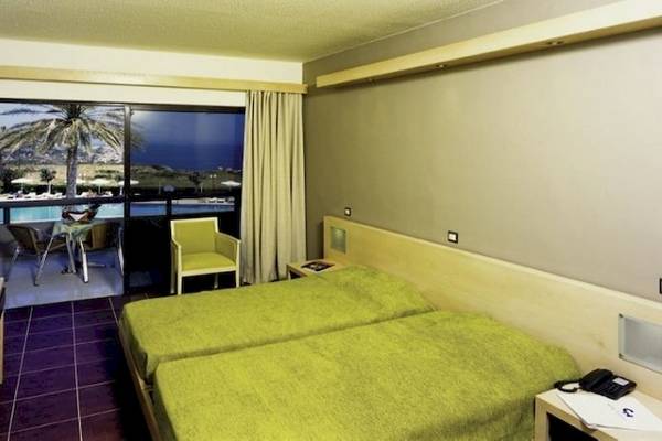 Doppelzimmer im Cathrin Hotel mit Blick auf den Pool und Palmen, inklusive zwei grünen Betten, einem Tisch, einem Stuhl und einem Fernseher.