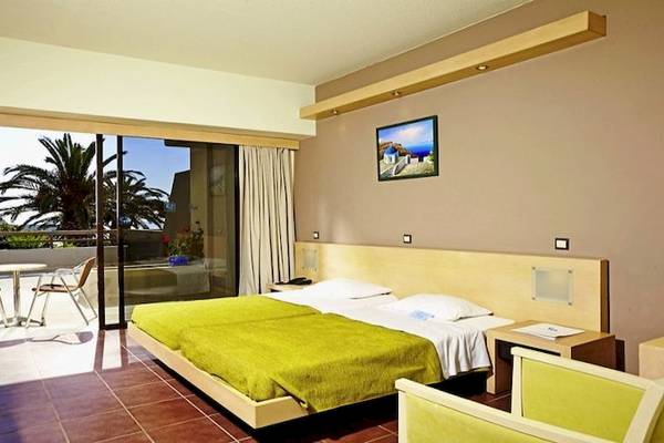 Hotelzimmer im Cathrin Hotel mit zwei Betten, grünen Decken, und einem Balkon mit Aussicht auf Palmen und Meer.