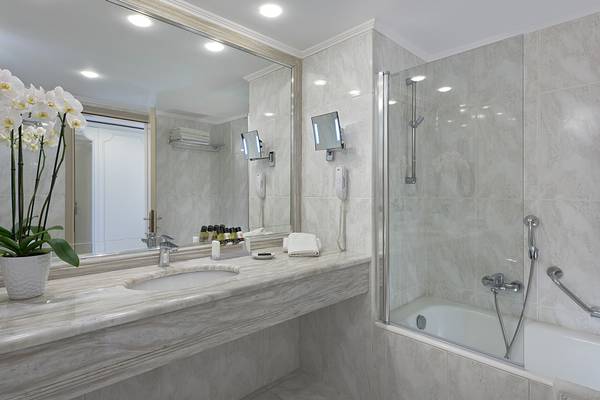 Badezimmer im Rodos Palladium Hotel mit Badewanne, Spiegel und Waschbecken.