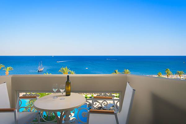 Balkon mit Meerblick im Rodos Palladium Hotel mit einem Tisch, zwei Gläsern und einer Flasche Wein.