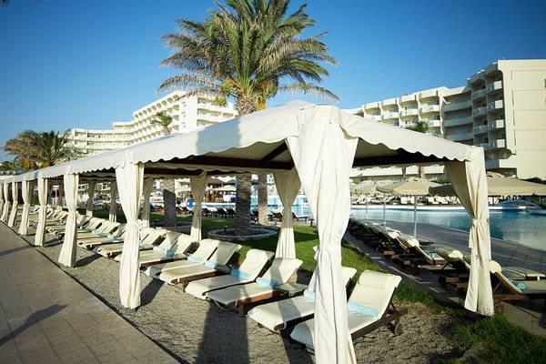 Reihe von Sonnenliegen unter einem großen Zelt im Freien neben einem Pool im Rodos Palladium Hotel.