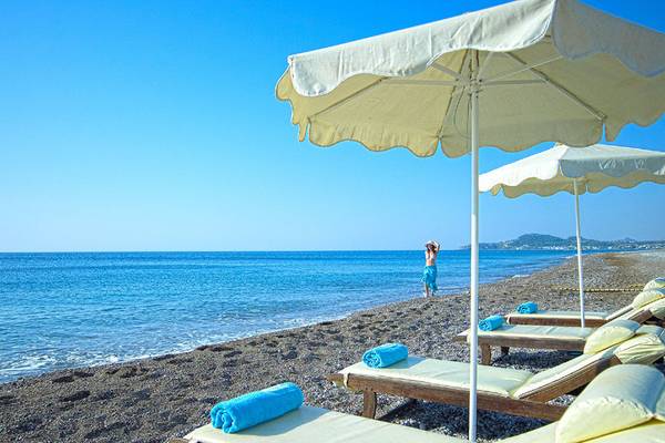 Strand mit Sonnenliegen und Umbrellas im Rodos Palladium, eine Person steht in der Ferne.