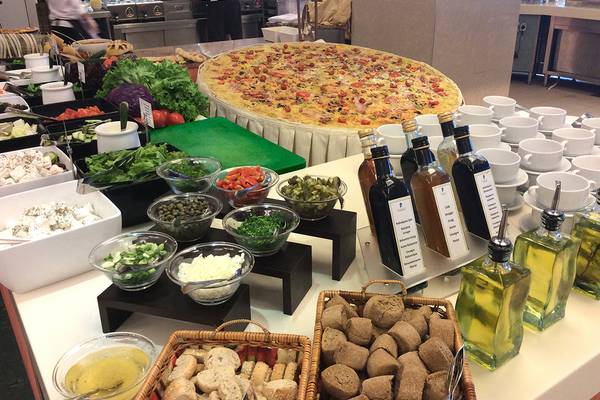 Große Pizza auf Buffettisch im Rodos Palladium Hotel mit verschiedenen Beilagen und Ölflaschen.